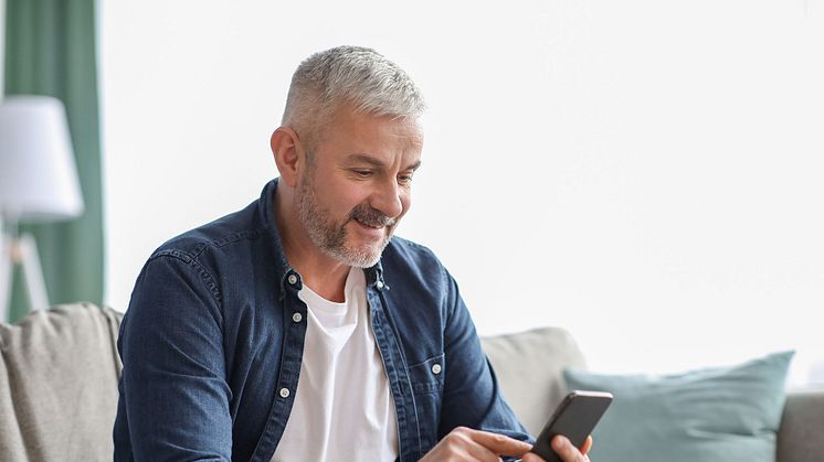 smiling senior man using smartphone while resting at home