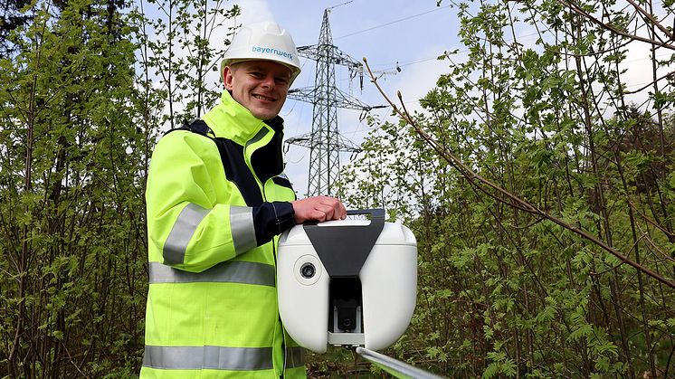 Bayernwerk-Techniker Thomas Schiml zeigt einen der schlauen Sensoren, die auf einer Hochspannungsleitung in Oberfranken montiert wurden. Unter anderem helfen Kamerabilder beim sicheren Netzbetrieb.