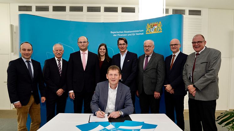 Michael Dümig von der Kommunalen Allianz Westspessart unterschreibt die Kooperationsvereinbarung im Beisein von Finanz- und Heimatminister Füracker (3. v.l.), Deutsche Glasfaser CEO Uwe Nickl (5. v.l.) und weiteren Vertretern der Allianz und DG.