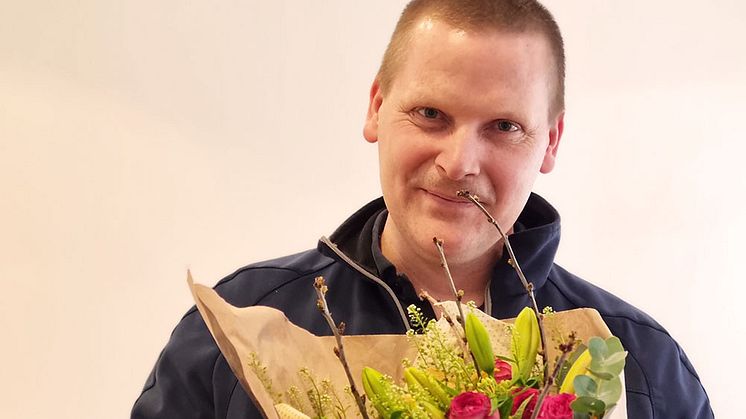 Fredrik Hermansson som är besiktningstekniker i Lysekil har utsetts till månadens medarbetare i Bilprovningen. På bilden gratuleras han med blommor och diplom.