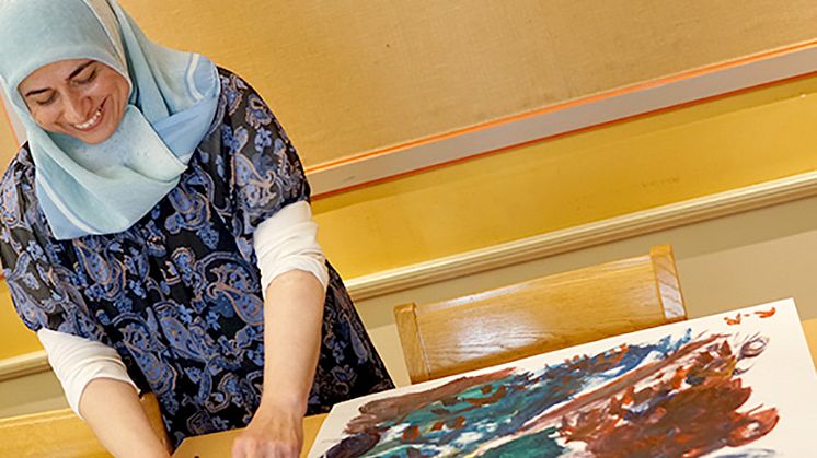 Syntolkning: Deltagare i projektet Rehabilitering med kultur står vid en teckning som hon just målat.