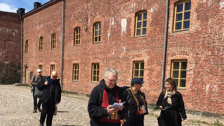 Kuvassa belgialainen zen-mestari Frank De Waele, säveltäjä Maija Kaunismaa ja pappi Maika Vuori tutustumassa sisällissodan aikaiseen vankileiriin Suomenlinnassa kesäkuussa 2017. Kuva Mikko Ijäs. 