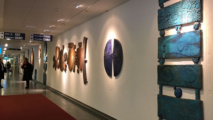 Syntolkning: Lindbergs keramiska gestaltning består av skisser i väggen och stora väggfasta objekt placerade längst en korridor i huvudentrén, Nacka sjukhus.