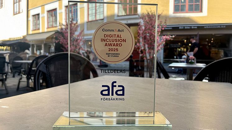 Priset i tävlingen CommToAct – Digital Inclusion Award 2025 står på ett ljusgrått bord med en äldre fasad i gult i bakgrunden