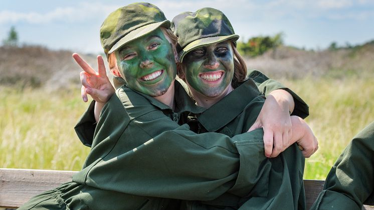 Två unga tjejer i grön overall och militärkeps kramas.