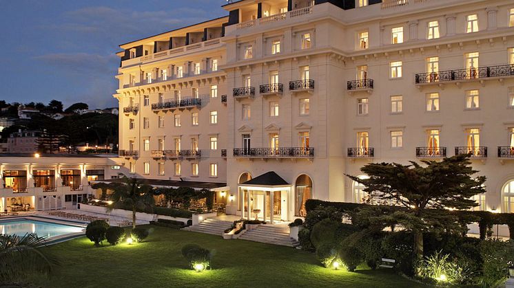 Hotel Palácio Estoril valaistuna iltahämärässä. Rakennus loistaa uljaana pimeässä ja viestii ylellisyyttä.