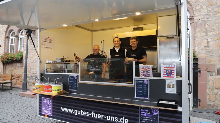 Heiko Otto und Natalija Smirnova, Hephata-Klient*innen (von links), mit dem Serviceleiter der Hessischen Landesvertretung in Berlin, Frank Schiller (Mitte), im Hephata-Imbisswagen auf dem Feierabendmarkt Alsfeld. Foto: Hephata Archiv/Melanie Schmitt