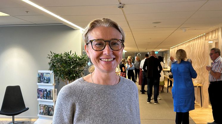 Lydia Kwak har en stickad grå tröja på sig, brunbågade glasögon, blont uppsatt hår och ler.