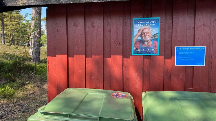 Affisch på en röd husfasad, två gröna sopkärl med stickers
