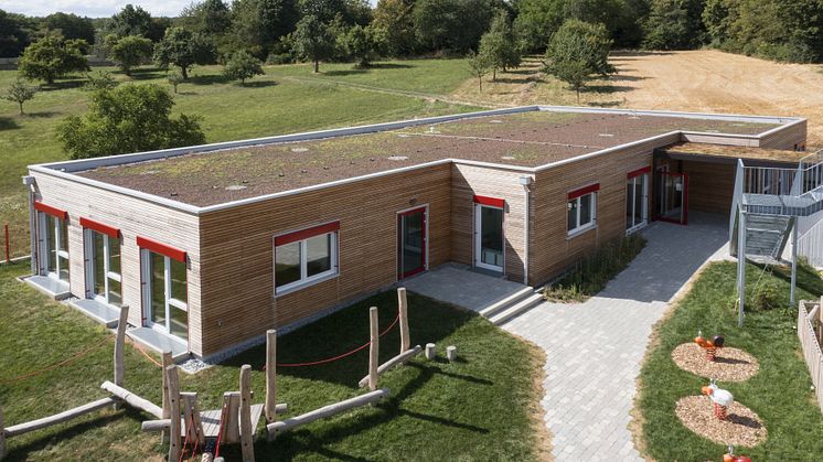 Die am Ortsrand von Walddorfhäslach gelegene Kita Herdweg passt sich aufgrund ihrer Holzfassade und dem begrünten Flachdach nahtlos der angrenzenden Umgebung mit Wiesen, Feldern und Bäumen an.