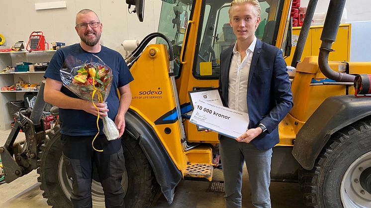 Mattias Askerson (M), ordförande utbildnings- och arbetsmarknadsnämnden överlämnar blommor och prischeck till Henrik Apell, platschef Sodexo Sigtuna. Pressbild: Sigtuna kommun 