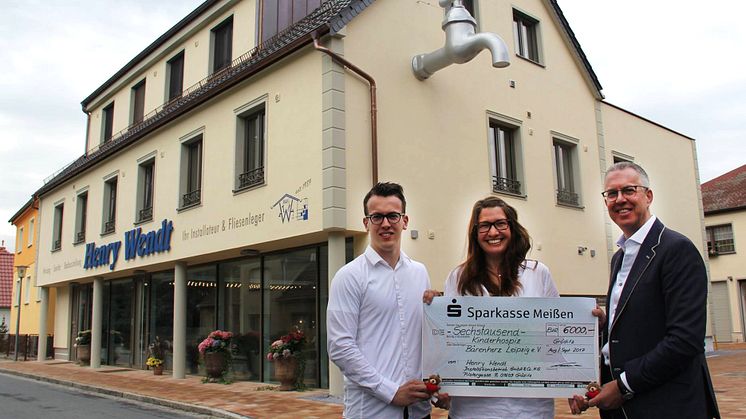 Hendrik Wendt, Ulrike Herkner und Henry Wendt mit dem Spendenscheck für Bärenherz vor dem neuen Geschäftshaus