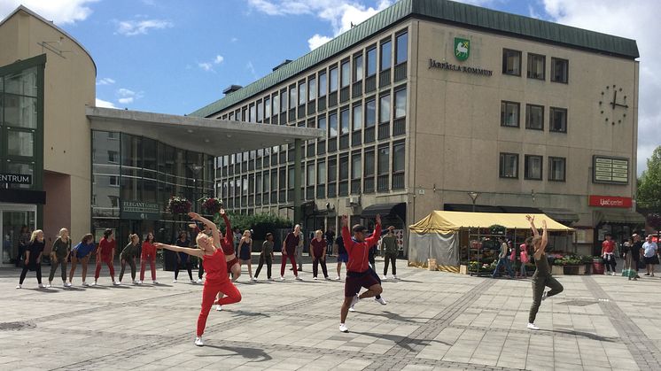DIS/Dans i Stockholms stad och län erbjuder ungdomar sommarjobb som dansare. Syntolkning: Rödklädda dansare uppträder på ett torg.  