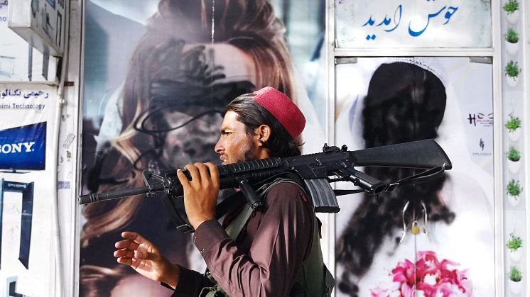En taliban passerar framför affischer där kvinnoansikten målats över.
