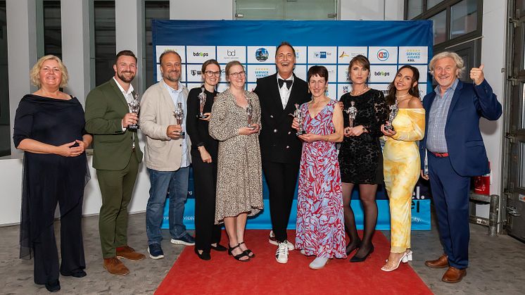 Björn Donner (Mitte mit Fliege) mit den Preisträger*innen des Service Award 2024, gerahmt von Stadtpräsidentin Bettina Aust und Uwe Wanger, Geschäftsführer Kiel-Marketing
