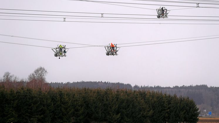 Hochspannungsmonteure arbeiten in speziellen Leitungsfahrwägen um Abstandshalter zwischen den Leiterseilen zu montieren. (Bernd Feil / LEW)