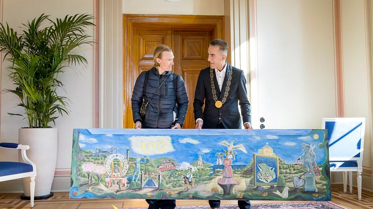 Konstnären Jeremia Håkan Andersson överlämnar en tavla till kommunfullmäktiges ordförande Aslan Akbas. Foto: Kristin Lidell