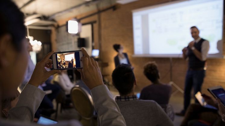 Businesswoman with camera phone videoing conference speaker in conference room