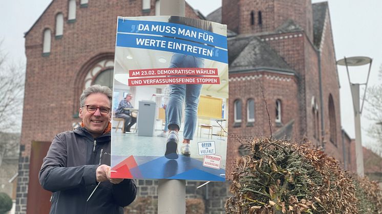 Hephata-Vorstandssprecher Maik Dietrich-Gibhardt bringt das Plakat mit dem Wahlaufruf von "Offen für Vielfalt" neben der Hephata-Kirche an. 