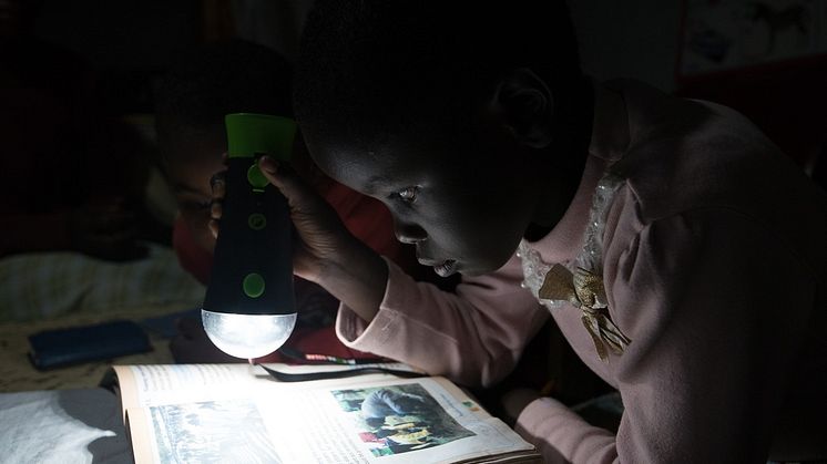 A child in Kenya is reading in the light from off-grid solarenergy. SunFunder borrower [Questworks / M-KOPA], Kenya
