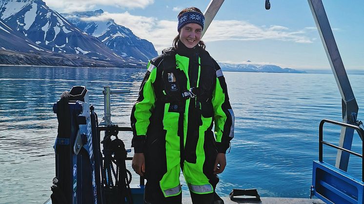 Forskare i grön och svart klädsel står på båtdäck i Svalbard.