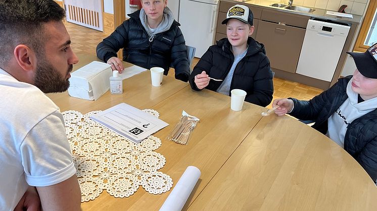 Vårdbiträdet Ahmad Alali visar August Davidsson, Texas Litzell och Gustav Östensson hur man matar en annan person.