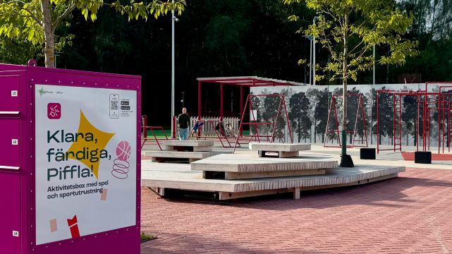 En rosa Piffl aktivitetsbox står placerad vid Rosendal allaktivitetsplats i Uppsala, omgiven av träd och lekytor.