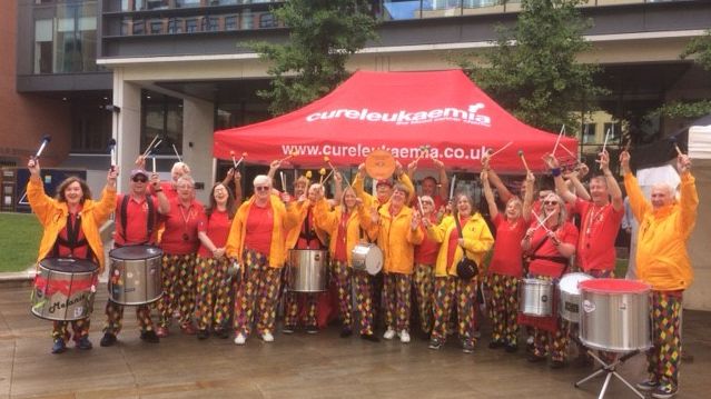 Someone at the Door Samba band playing in Brindley Place with their Cross City Heroes plaque