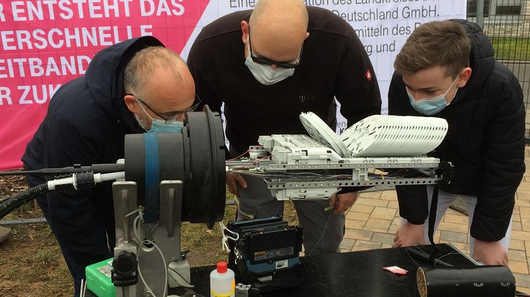 Foto: Dr. Benfer - Landrat Daniel Kurth und Schüler Ian schauen einem Telekom-Techniker beim Spleißen von Glasfaser vor der Oberschule Schwanebeck zu