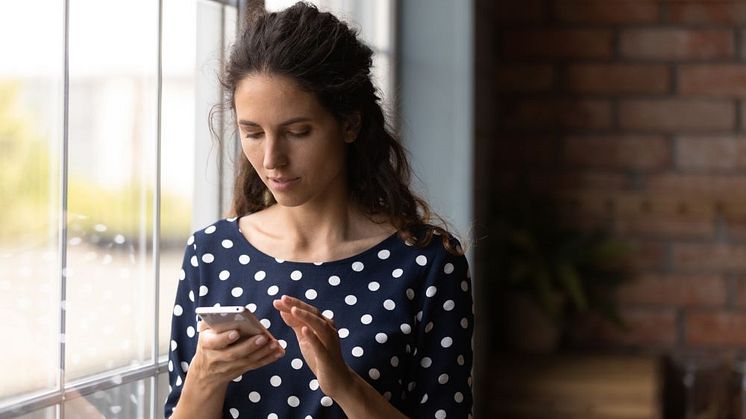 Syntolkning: Kvinna som tittar på en mobiltelefon.