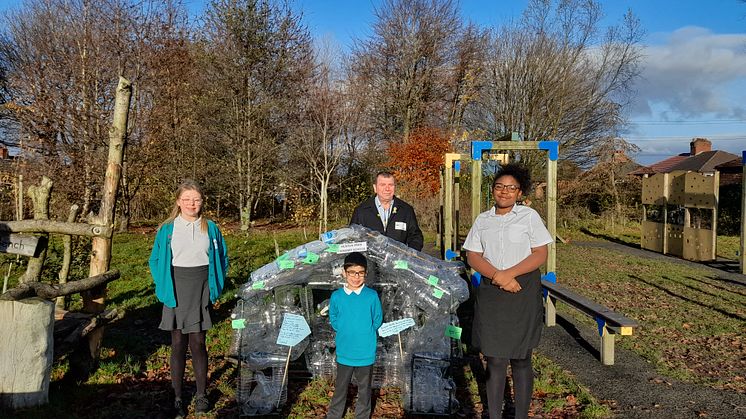 Cllr Alan Quinn with students from Heaton Park Primary school in front of their greenhouse artwork made of plastic bottles