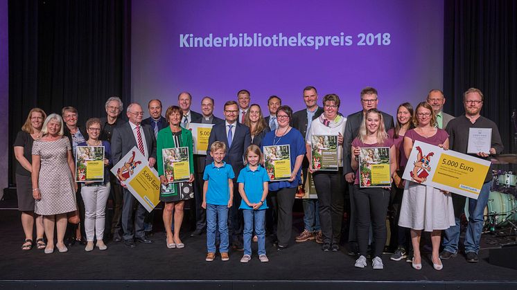Gemeinsame Preisverleihung, doppelte Freude: Die fünf Gewinner-Büchereien des Kinderbibliothekspreises 2018 strahlen beim Siegerfoto im AURELIUM Lappersdorf mit dem diesjährigen Paul-Maar-Preisträger Jens Raschke (r.) um die Wette.
