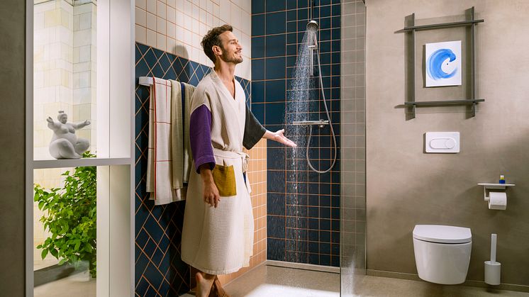Ein Mann steht mit einem Bademantel in der Dusche und halt seine Hand in den Wasserstrahl einer Handbrause von Hansgrohe