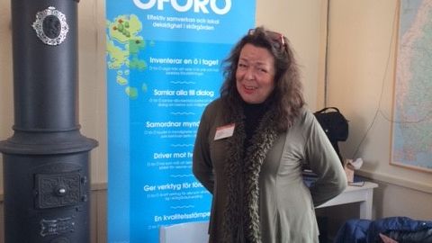 Irene Book är initiativtagare till Kultur på Sandhamn. Syntolkning: Irene står framför en roll-up med texten ”Ö för ö”. Foto: Kajsa Bellander 