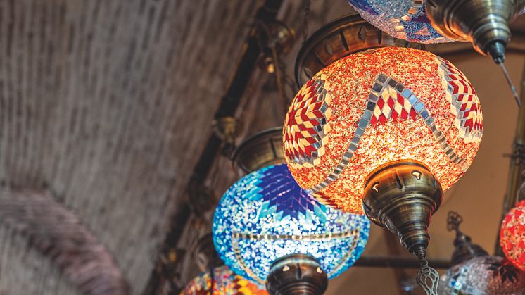 Kuva värikkäistä mosaiikkilampuista, jotka roikkuvat tiiliholvikatosta. Lampuissa on monivärisiä, koristeellisia kuvioita