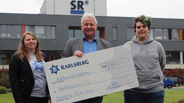 Die Karlsberg-Auszubildenden Melanie Schunk (links) und Leonie Roos (rechts) übergaben den Spendenscheck an Thomas Rosch vom Saarländischen Rundfunk. Foto: Karlsberg
