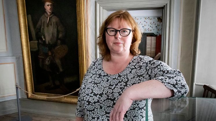 Annika Windahl Pontén standing in front of a portrait of Carl Linnaeus.