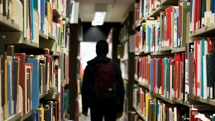 En kille med ryggsäck går ensam i ett bibliotek.