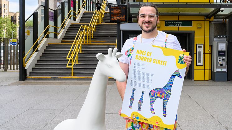 Artist, Aaron Bevan, poses outside of East Croydon station with one of the giraffe sculptures 