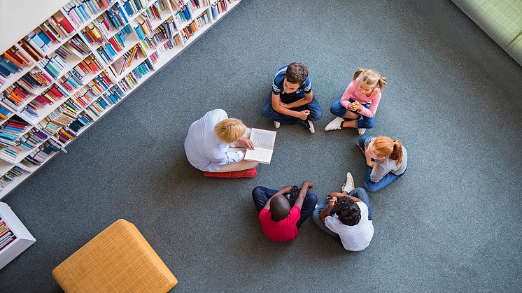 Syntolkning: Barn lyssnar på vuxen som läser bok 