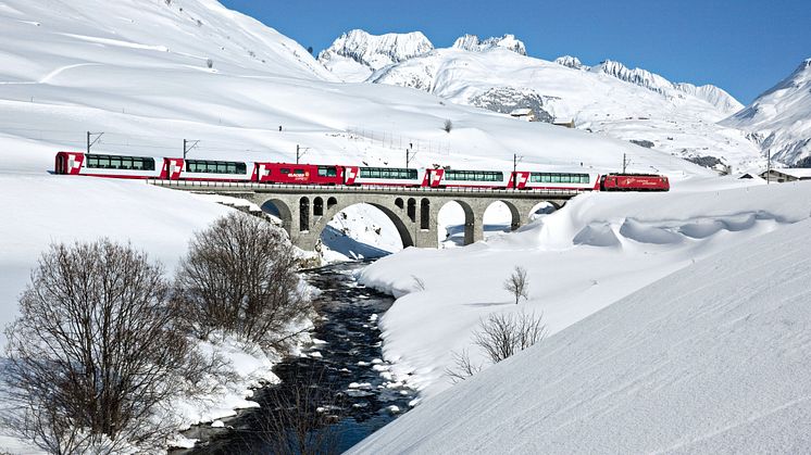 Der Glacier Express überquert im zugeschneiten Urserental in der Nähe des Dorfes Hospental im Kanton Uri die Furkareuss 