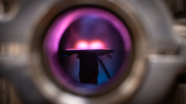 En titt in i vakuumkammaren där man ser plasmat ovanför ytan där metallfilmen skapas.