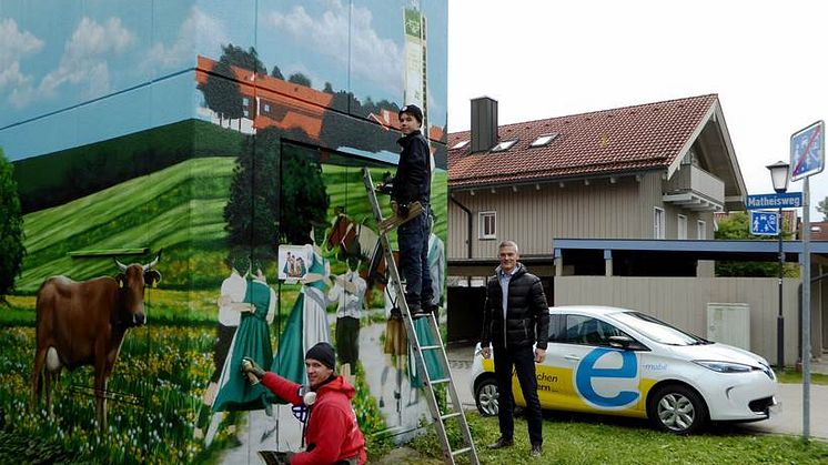 Heimatverbundenheit ziert Turmstation: Bayernwerk-Kommunalbetreuer Alexander Usselmann (rechts) besuchte die Art-EFX-Künstler Markus Ronge (links) und Pascal Sturm (Mitte) bei der Fertigstellung des Kunstwerks in Otterfing.