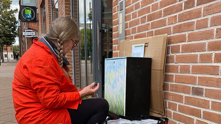 Konstnären Ann-Christine Jönsson sitter på plats på Mårtensgatan i Kävlinge och målar vackra grässtrån på ett elskåp. Fotograf: Monika Carnehult