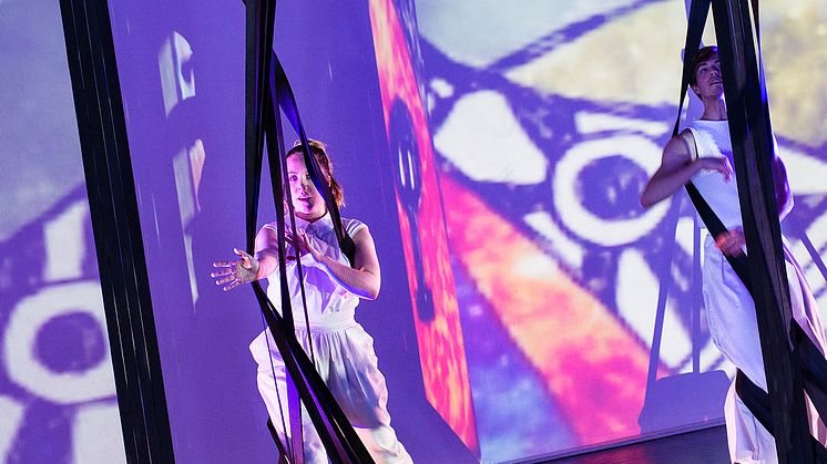 Ur dansföreställningen Sannolikt, osannolikt (2017) av koreografen Christina Tingskog.  Foto: Anna Molander. Syntolkning: Två dansare står bland hängande rep och ljusprojektioner. 
