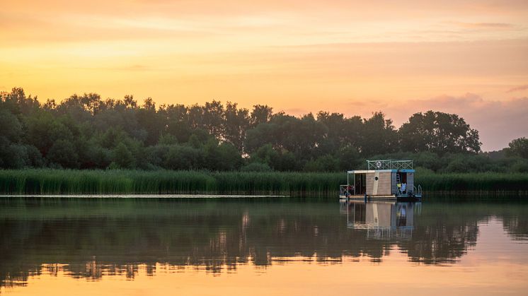 Ein_Hausbootes_im_See_bei_Sonnenuntergang_in_Brandenburg