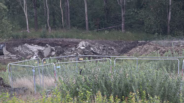Området för den planerade reningsdammen består av lera och gyttja. Platsen där en grävmaskin sjönk och välte är inhägnad med byggstängsel. Bild tagen med teleobjektiv eftersom kyrkogårdsförvaltningen inte tillåter fotografering inne i arbetsområdet.
