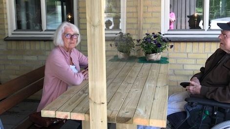 Äkta makarna Birgitta Och Claes Lagerlund vid mötesbänken med plexiglasskiva utanför vård- och omsorgsboendet Ålycke i Johannishus