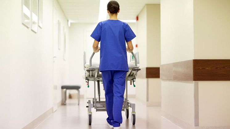 Vårdanställd skjuter på en bår i en sjukhuskorridor med ryggen vänd mot kameran 