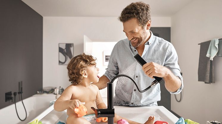 Ein Kind wird in einem modernen Waschtisch gebadet. Die neue Armatur von hansgrohe hat einen Schlauch.